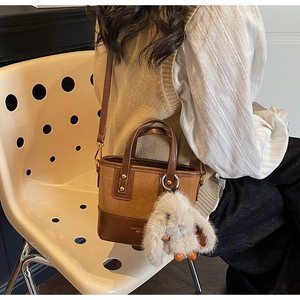 Détail d'un sac seau marron aux textures mixtes, breloque lapin en peluche et bandoulière