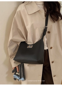Close-up of black litchi leather shoulder bag with silver twist lock on beige coat