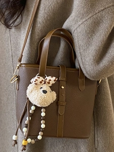 Minimalist brown pebbled leather bucket bag with plush bear charm and crossbody strap