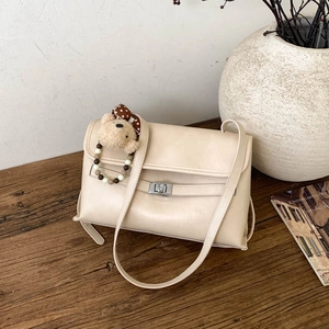 Detail of cream crossbody bag with silver twist lock and cute plush bear charm on wood