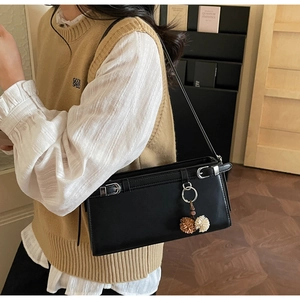 Detail of black rectangular crossbody bag with silver buckles and floral ball pendant