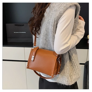Detail of a brown lychee pattern leather crossbody bag with silver buckle on a model