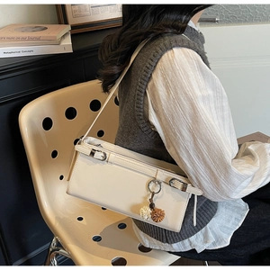 Detail of a creamy white leather baguette bag with fur pompom charm and thin shoulder strap