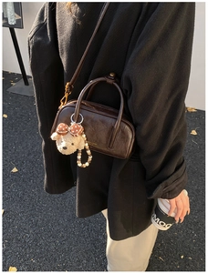 Détail d'un sac bowling marron café avec breloque ours et logo doré porté à l'épaule