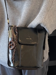 Fashionable black bucket shoulder bag in glossy leather with gold charms on a grey sweater
