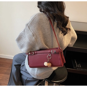 Burgundy rectangular shoulder bag with silver buckle straps and fluffy charm shown on model