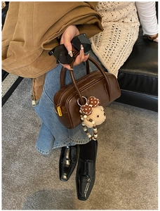 Détail d'un sac bowling en cuir marron avec fermeture éclair dorée et charm ours en peluche