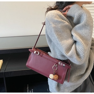 Close-up of a burgundy leather baguette bag with silver buckles and a floral pendant