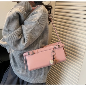 Pink faux leather shoulder bag with silver buckle and plush pompom on gray sweater