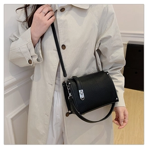 Close-up of black lychee leather bag with silver metal lock on a beige trench coat