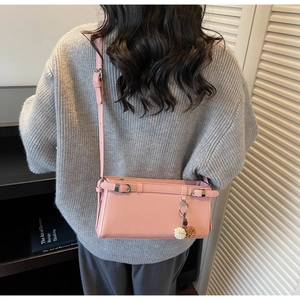 Detail of pink faux leather crossbody bag with decorative metal buckle and pom-pom charm