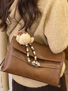 Vintage dark brown tote bag with bear charm and beaded chain on a beige knitted sweater