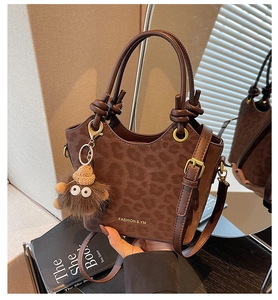 Détail du sac seau marron foncé à motif léopard avec breloque monstre et logo doré