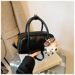 Gros plan du sac bowling noir en cuir huilé brillant avec breloque chien en peluche et métal doré