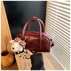 Détail du mini sac bowling bordeaux avec texture brillante et pendentif ours en peluche