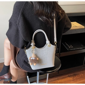 Close-up of a grey bucket bag with a gold logo and a cute brown plush monster charm