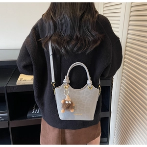 Detail of grey leopard bucket bag with plush charm and gold hardware on a model