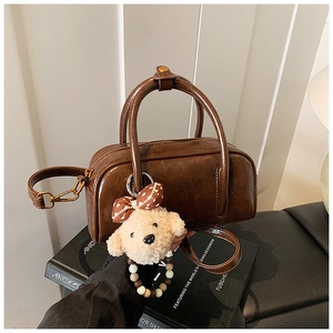 Détail du sac bowling marron brillant avec garniture dorée et breloque en peluche