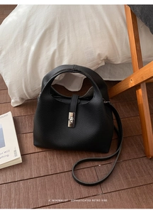 Detail of black lychee grain leather bucket bag with silver metal twist lock on wood