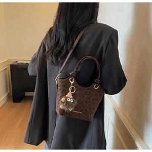Detailed view of leopard print bucket bag with plush monster charm and shoulder strap