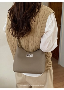 Close-up of a taupe leather bucket bag featuring a silver twist lock and lychee texture