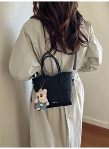 Détail d'un sac seau en cuir noir avec un porte-clés ours en peluche porté par un mannequin