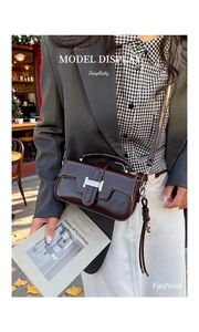 Close-up of a dark brown glossy leather crossbody bag with a silver H-shaped metal buckle