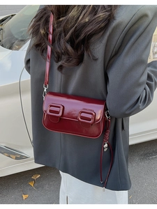 Close-up of a deep red glossy leather saddle bag featuring dual large square buckles