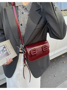 Detailed macro view of glossy dark red saddle bag with fringe charm and square buckles