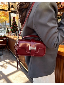 Chic burgundy leather crossbody bag with silver buckle worn by a model in a cozy cafe