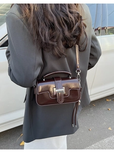Detail view of dark brown patent leather square bag with silver metal buckle in a street setting