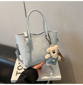 Détail du sac seau en cuir bleu clair avec bandoulière réglable et breloque ours en peluche