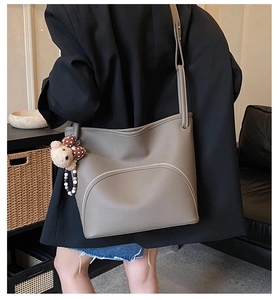 Detail of taupe pebbled leather tote featuring white stitching and bear charm accessory