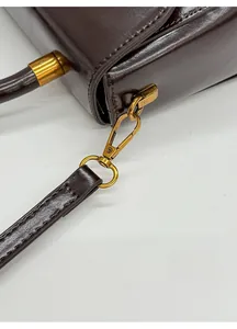 Detail of detachable bronze lobster clasp and stitching on dark brown leather bag