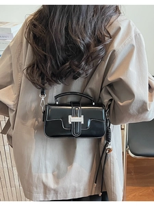 Detail view of black patent leather crossbody bag with silver buckle and woven strap