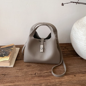 Close-up of grey litchi grain leather bucket bag with silver twist lock on wooden surface