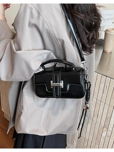 Close-up of black leather crossbody bag with silver buckle and braided tassel detail