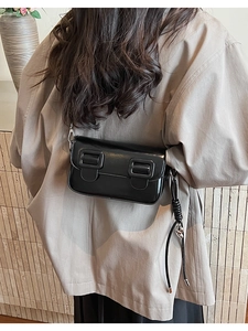 Detail view of black glossy saddle bag with silver hardware and woven strap detail