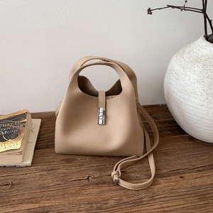 Close-up of beige leather bucket bag with silver lock and fine litchi grain texture