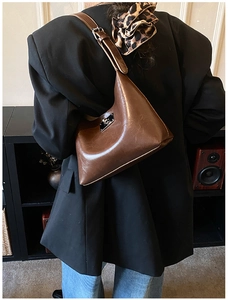 Detail of vintage brown leather underarm bag with silver buckle worn with a black blazer
