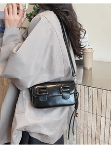 Detail of a black glossy leather crossbody saddle bag with twin square buckles and tassels
