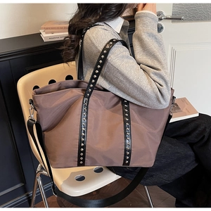 Close-up of brown tote bag showing black leather strap with silver rivets and metal hardware