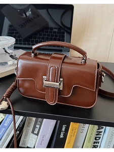 Detail view of glossy dark brown leather handbag on office desk with lifestyle props