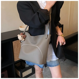 Close-up of taupe litchi grain leather tote bag featuring white zipper and cute bear charm