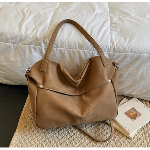 Close-up of khaki PU leather tote bag with embossed daisy pattern on a straw mat