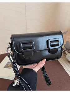 Close-up of black leather crossbody bag with square buckles and silver heart pendant