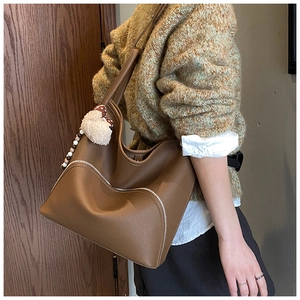 Detail view of brown pebbled leather tote bag with side zipper and cute plush bear charm