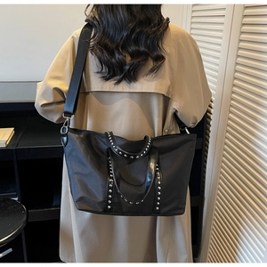 Detail of a black large tote bag with silver studs worn by a model in a trench coat