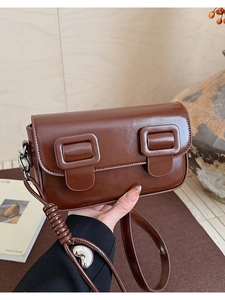 Detail of dark brown glossy saddle bag with square buckles and silver heart pendant
