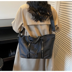 Close-up of black tote bag featuring silver studs and adjustable wide shoulder strap detail